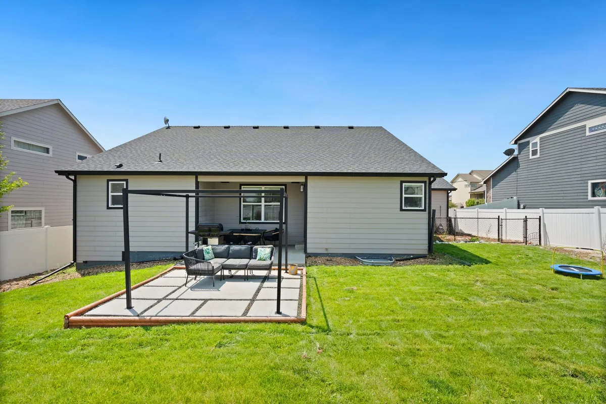 Backyard patio with a steel pergola and outdoor seating beside a fenced green lawn