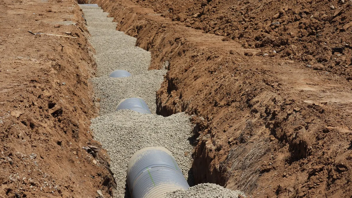 Corrugated drain pipe bedded in clean gravel along the bottom of a freshly dug trench