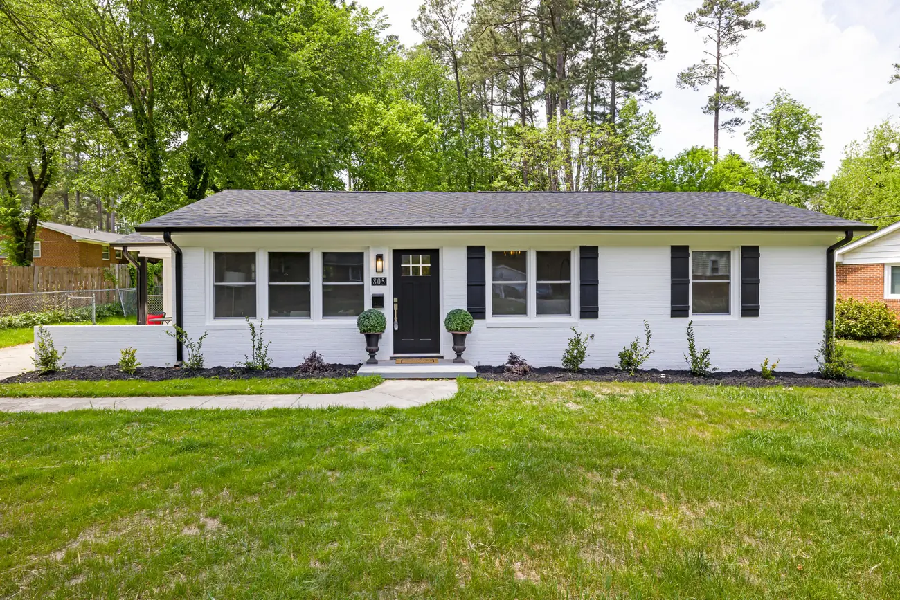Single-story white brick home with freshly mulched planting beds, trimmed shrubs and a wide green front lawn