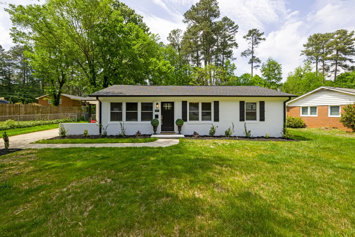 Single-story white house with clipped foundation shrubs and a sloping, well-kept front lawn