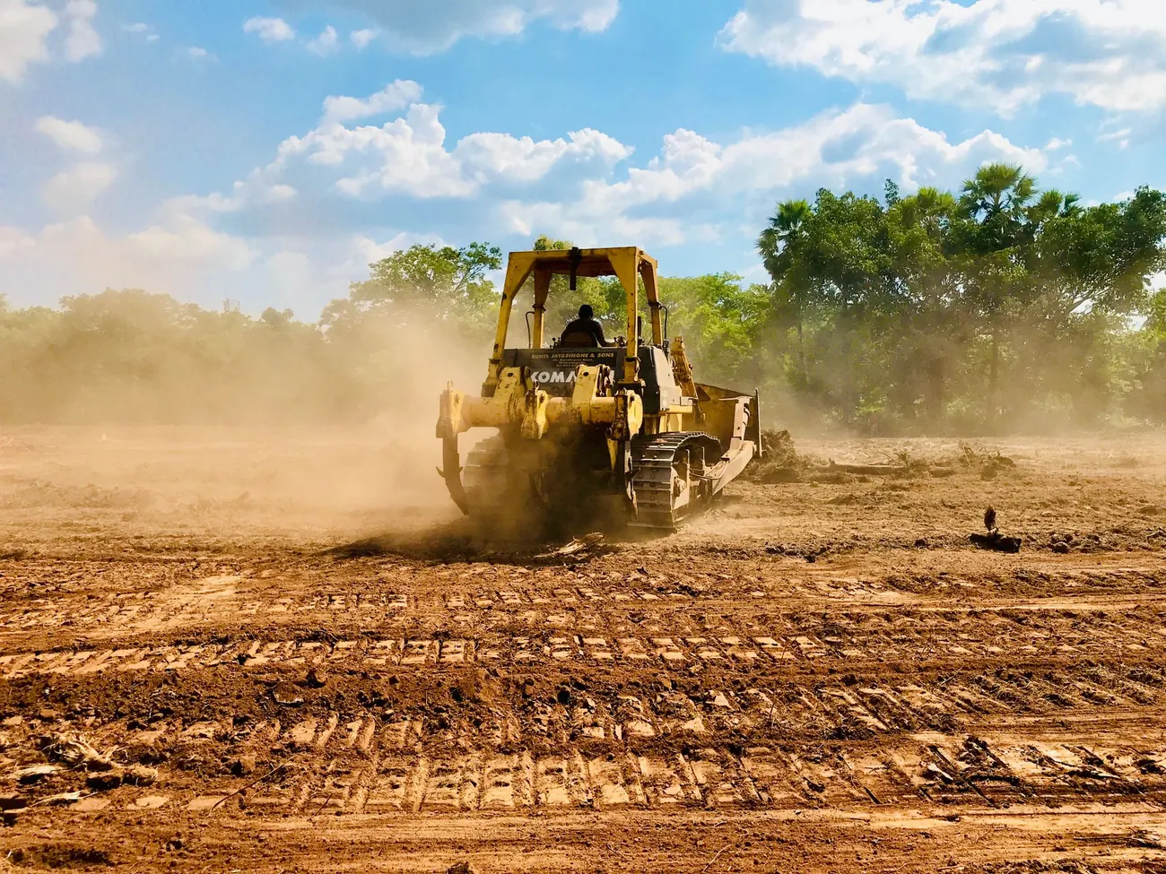 Bulldozer pushing soil across a cleared lot, grading the ground on a dry, dusty day