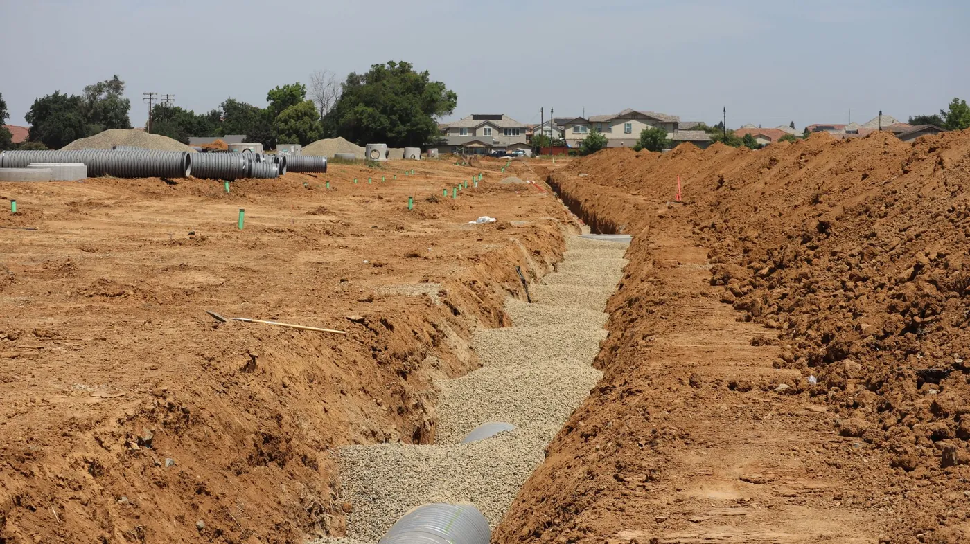 Open drainage trench and sections of large concrete storm pipe on a residential development site